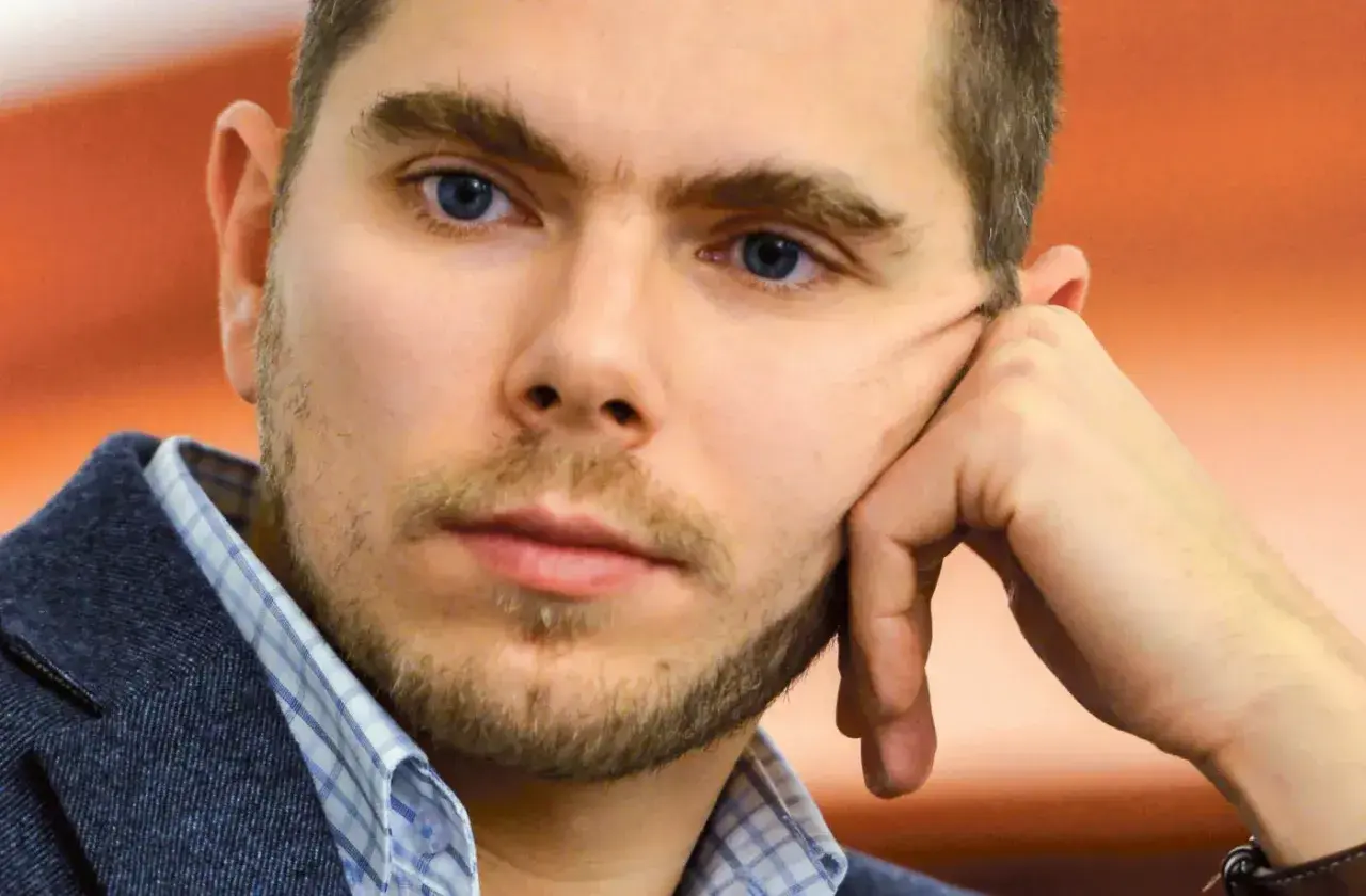 Portret Piotra Zychowicza, mężczyzny z niebieskimi oczami, opierającego głowę na dłoni.